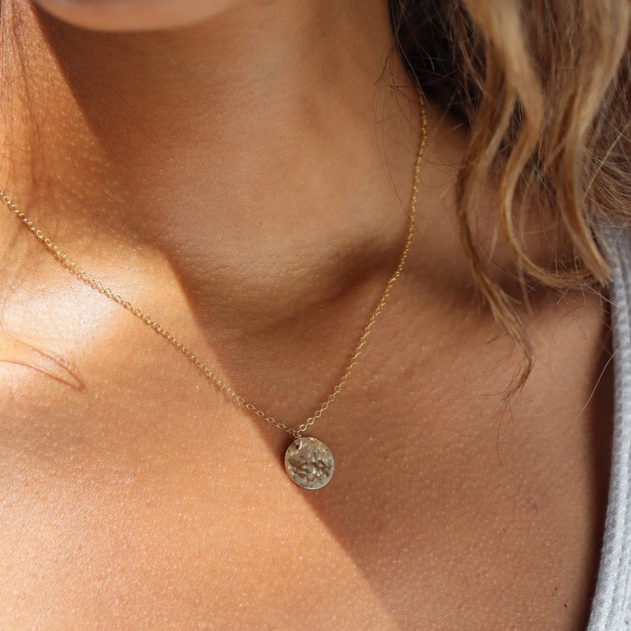 Model wearing 14k gold fill Moon drop necklace in the sunlight. This necklace features our simple chain met by a hammered coin, making it look like the moon.