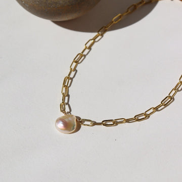 14k gold fill Anklet featuring a freshwater pearl, laid on a white paper in the sunlight.