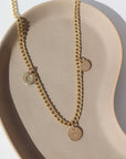 14k gold fill Modern Muse Initial Necklace laid on a tan plate in the sunlight. This Necklace feature our Demi Alexandra chain featuring a charm initial of your choice.
