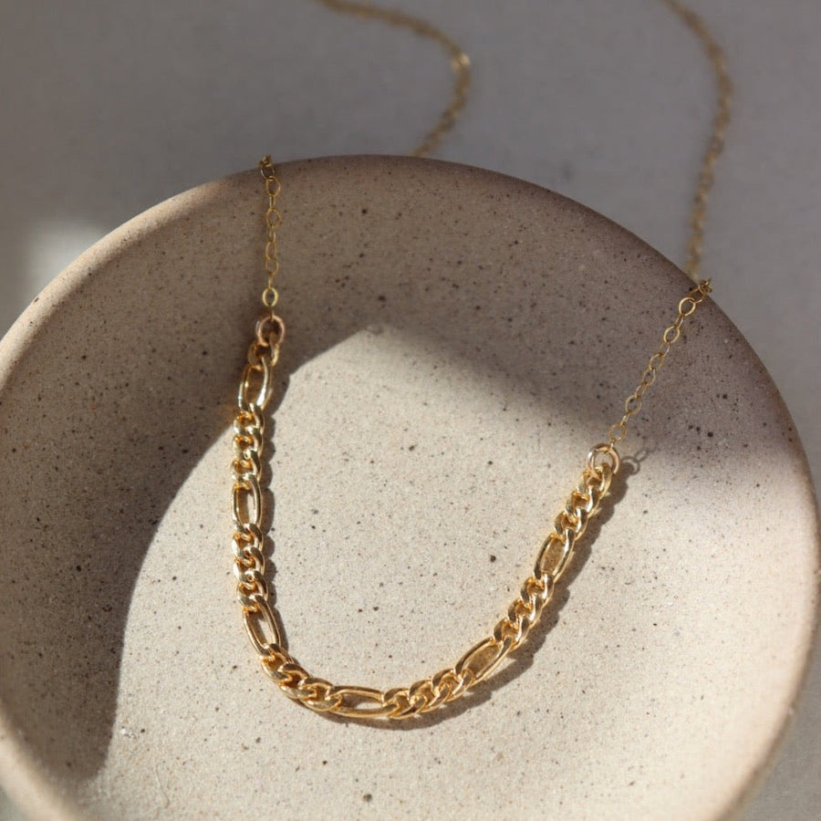 gold Figaro chain combined with a delicate cable chain and sitting on a jewelry dish in the sun