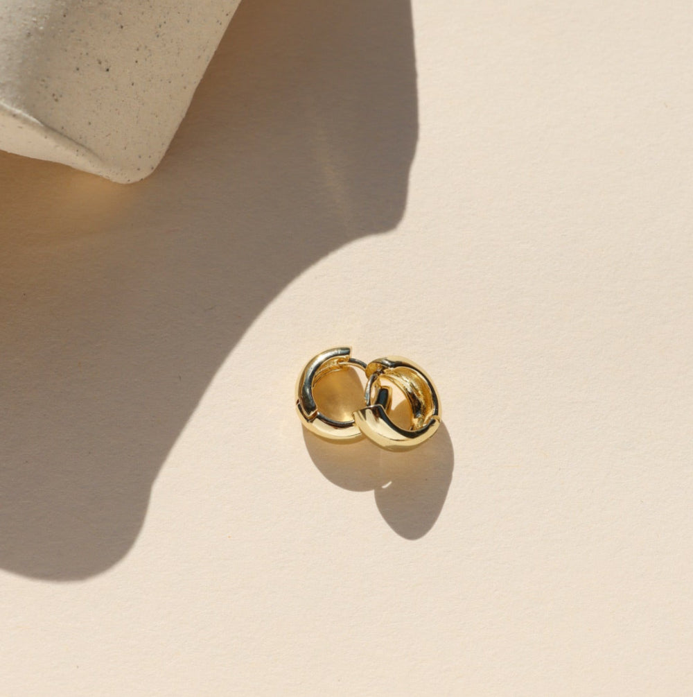 Gold earring on a beige surface with a soft shadow