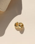 Gold earring on a beige surface with a soft shadow
