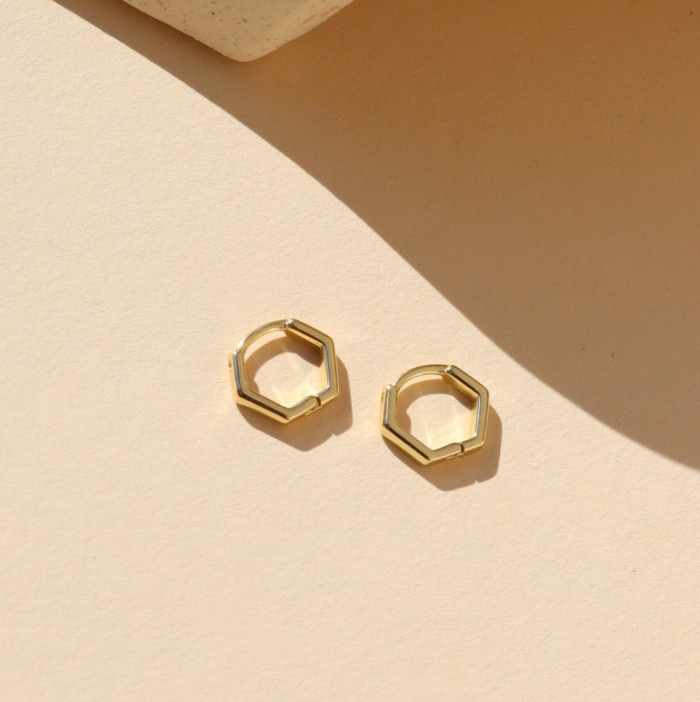 Gold hexagonal stud earrings on a beige background