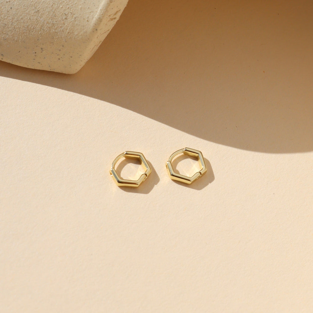 Gold hexagonal hoop earrings on a beige background