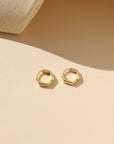 Gold hexagonal hoop earrings on a beige background