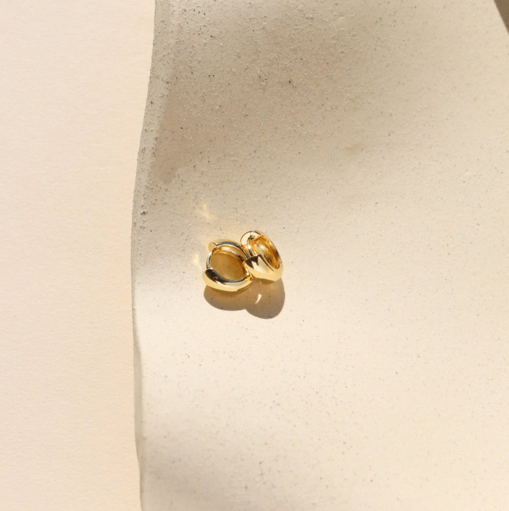 Gold earring on a white cushion against a beige background