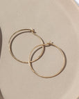 14k solid gold Organic Hoops by Token Jewelry. The hoops are a circle shape with hammered solid gold wire, photographed on a tan ceramic dish