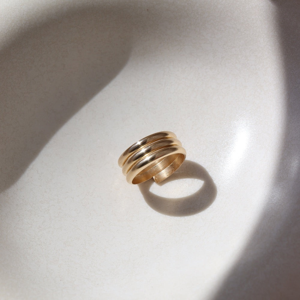 14k gold fill Trinity ring spirals into three bands, photographed on a white sunlit ceramic dish.This ring features the look of the three layered band look but its only one ring.