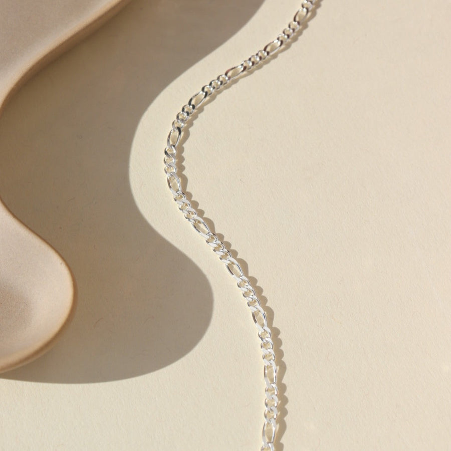 925 sterling silver Gio chain laid on a tan paper in the sunlight.