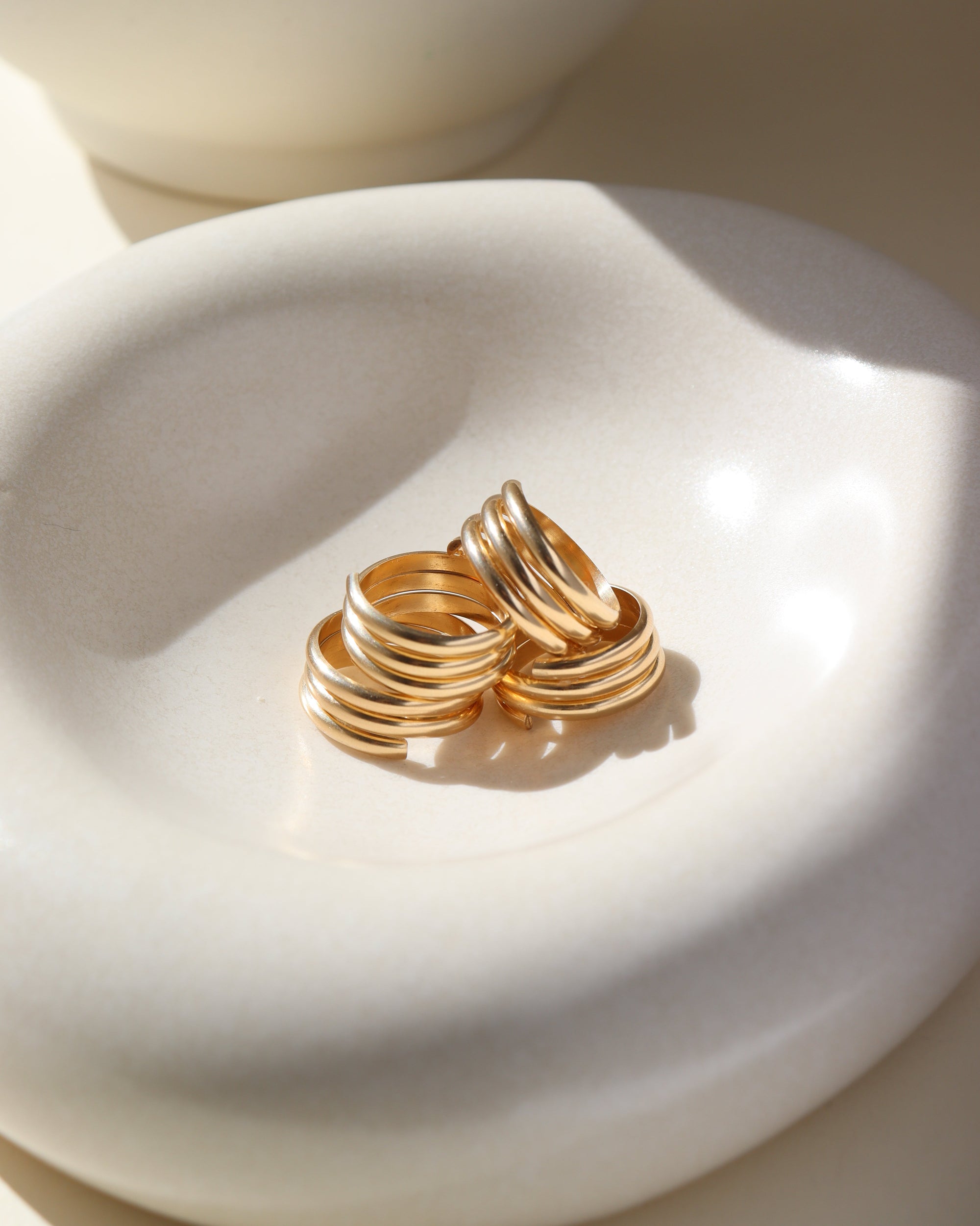 14k gold fill Trinity ring spirals into three bands, photographed on a white sunlit ceramic dish.This ring features the look of the three layered band look but its only one ring.