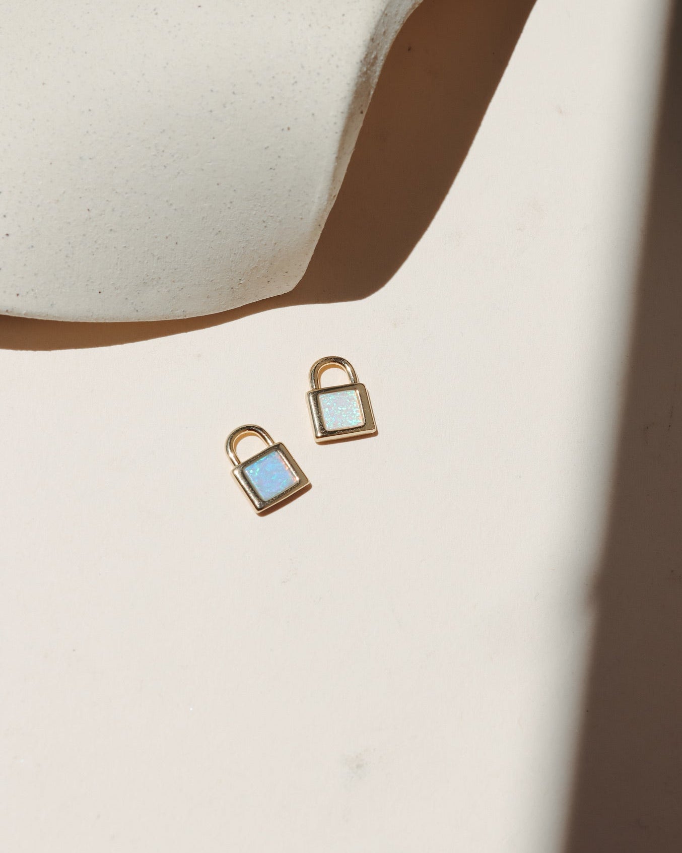 Gold padlock charm with shimmering white and blue opal stones on a neutral surface in warm natural light.