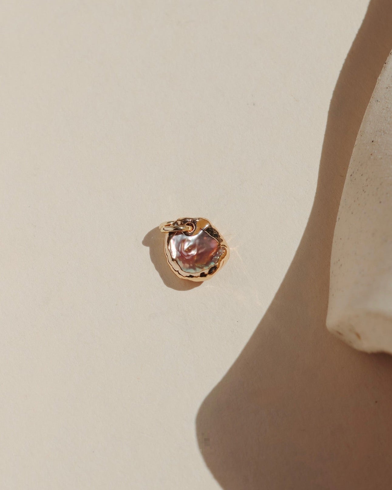 Organic keshi pearl charm with gold foil edging photographed in warm natural light.