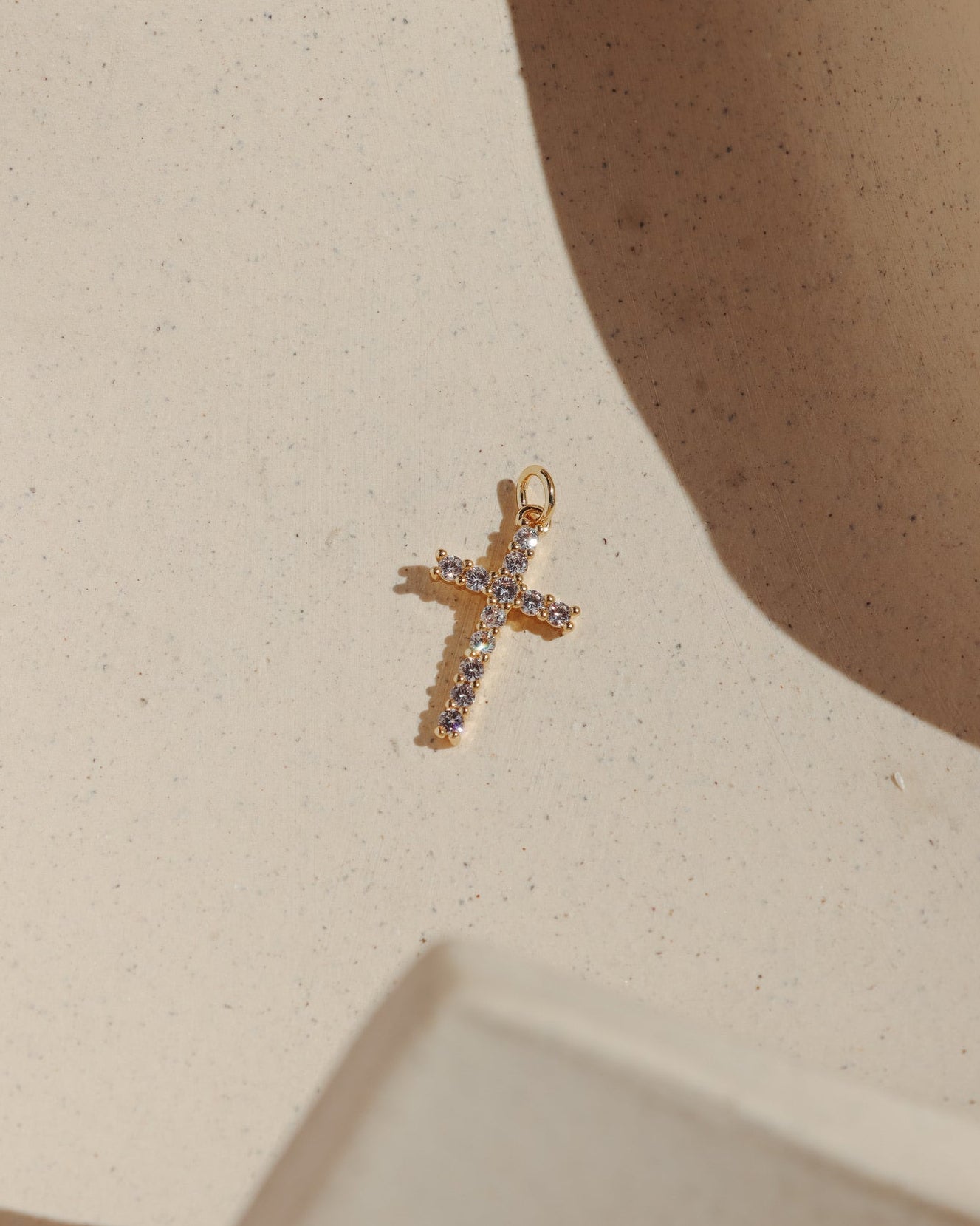 Gold cross charm set with sparkling pavé stones on a neutral background.