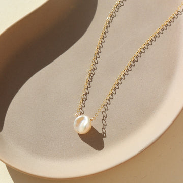 14k gold fill freshwater pearl necklace laid on a peach colored plate. This necklace features the simple chain with the freshwater pearl  wired in the middle.