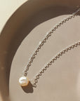 925 sterling silver freshwater pearl necklace laid on a peach colored plate. This necklace features the simple chain with the freshwater pearl wired in the middle.
