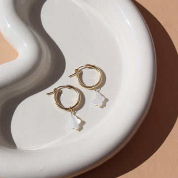 mother of pearl Butterfly shaped charms hanging from a small 14k gold fill hoop earring, photographed on a white curved ceramic dish