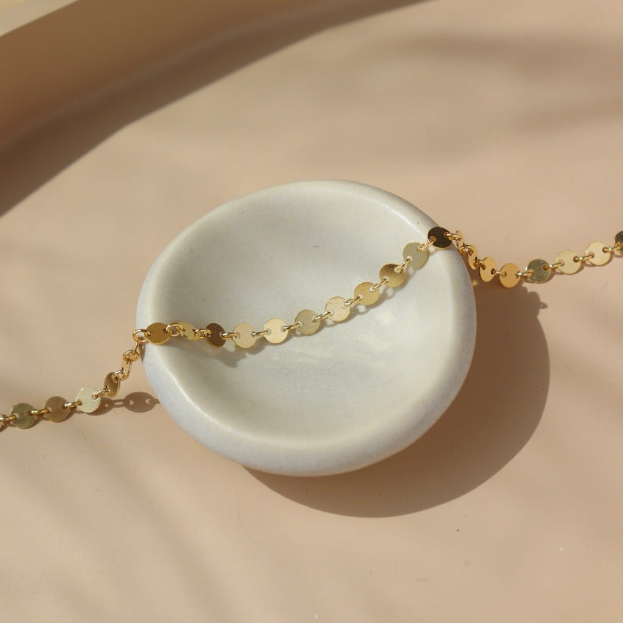 14k gold filled disc chain connected with small jump rings, photographed draped over a white ceramic plate on a tan tabletop