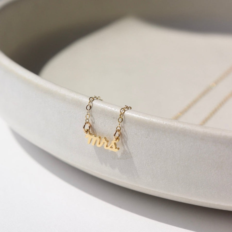 14k gold fill Mrs.Necklace laid on a white jewelry dish in the sunlight.  This is perfect to gift any bride to be in your life.