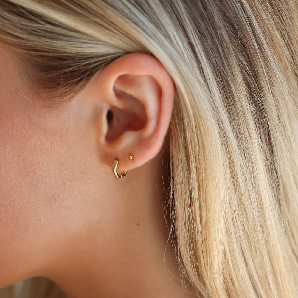 Close-up of an ear wearing a gold earring with blonde hair.