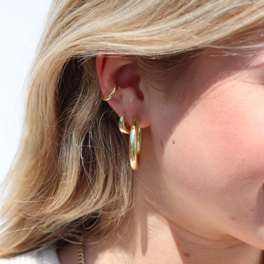 Model wearing 14k gold fill Harper hoops. These earrings feature a classic smooth hoop with a post making the easy to take in and out.