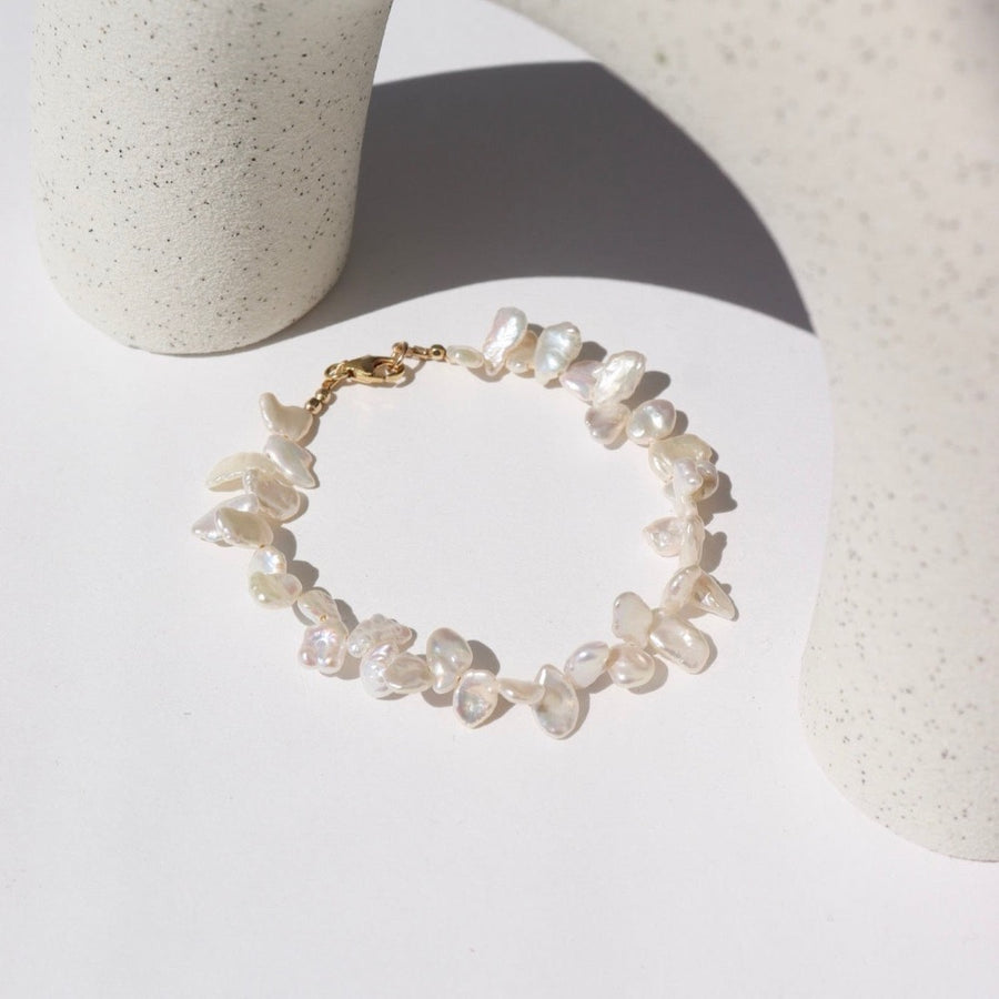 14k gold fill Pearl Petals Bracelet laid on a white paper in the sunlight.