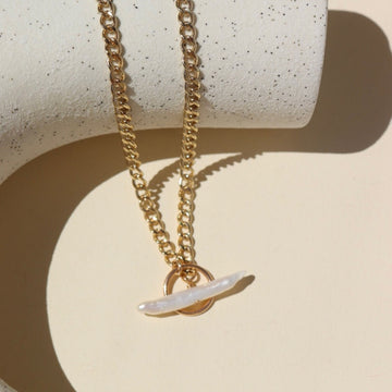 14k gold fill Demi Alex Toggle w/ pearl laid on a white paper in the sunlight.