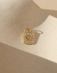 Gold rectangular playing card charm with a textured finish and pavé heart center, photographed on a neutral stone surface in warm natural light.