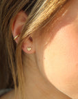 dainty gold heart earring with a patterned border, pictured on a model in sunlight