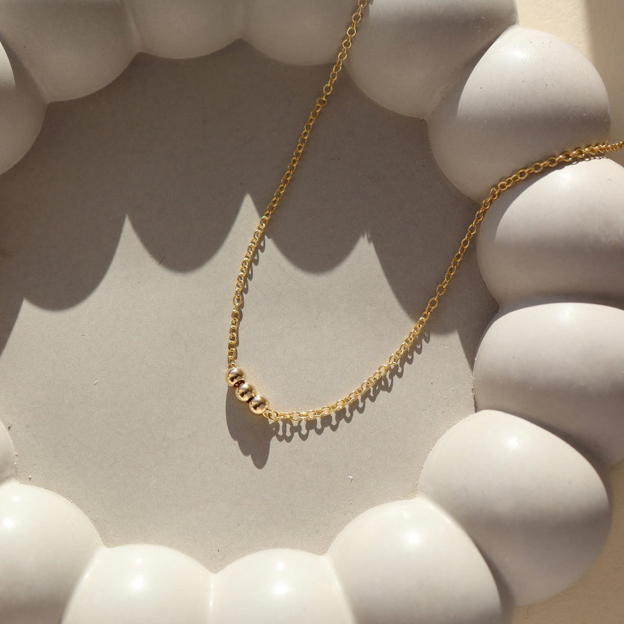 three small beads on a gold chain made by Token Jewelry