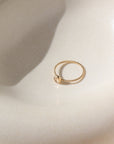 14k gold fill Gaia Ring laid on a white plate in the sunlight. This ring features a Spiral band with a zircon gemstone.