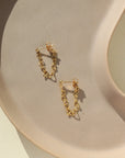 a heart chain on stud earrings, photographed on a sunlit ceramic dish