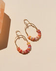 Gold hoop earrings with colorful beads on a beige background