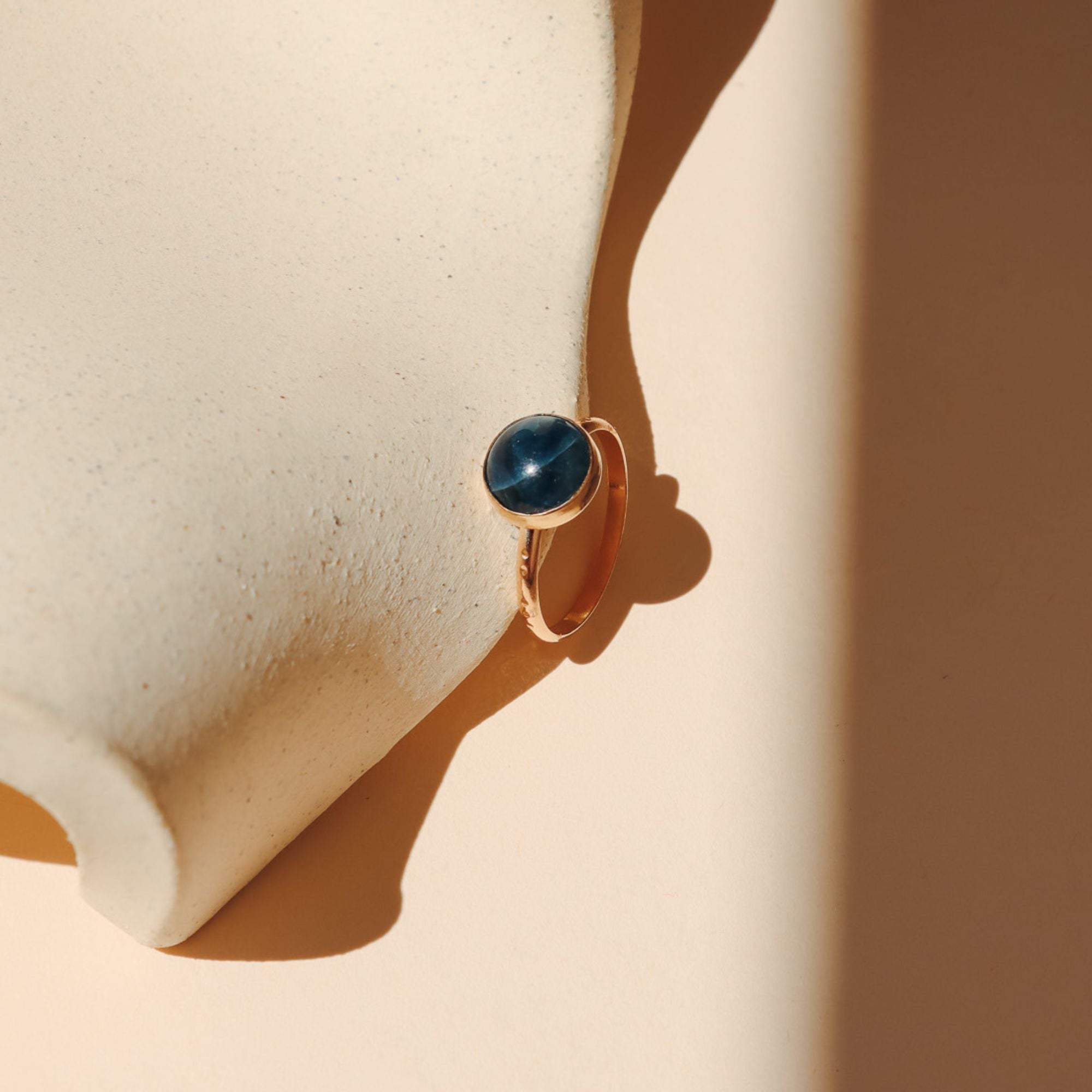 14k gold fill ring with round blue stone on a light dish