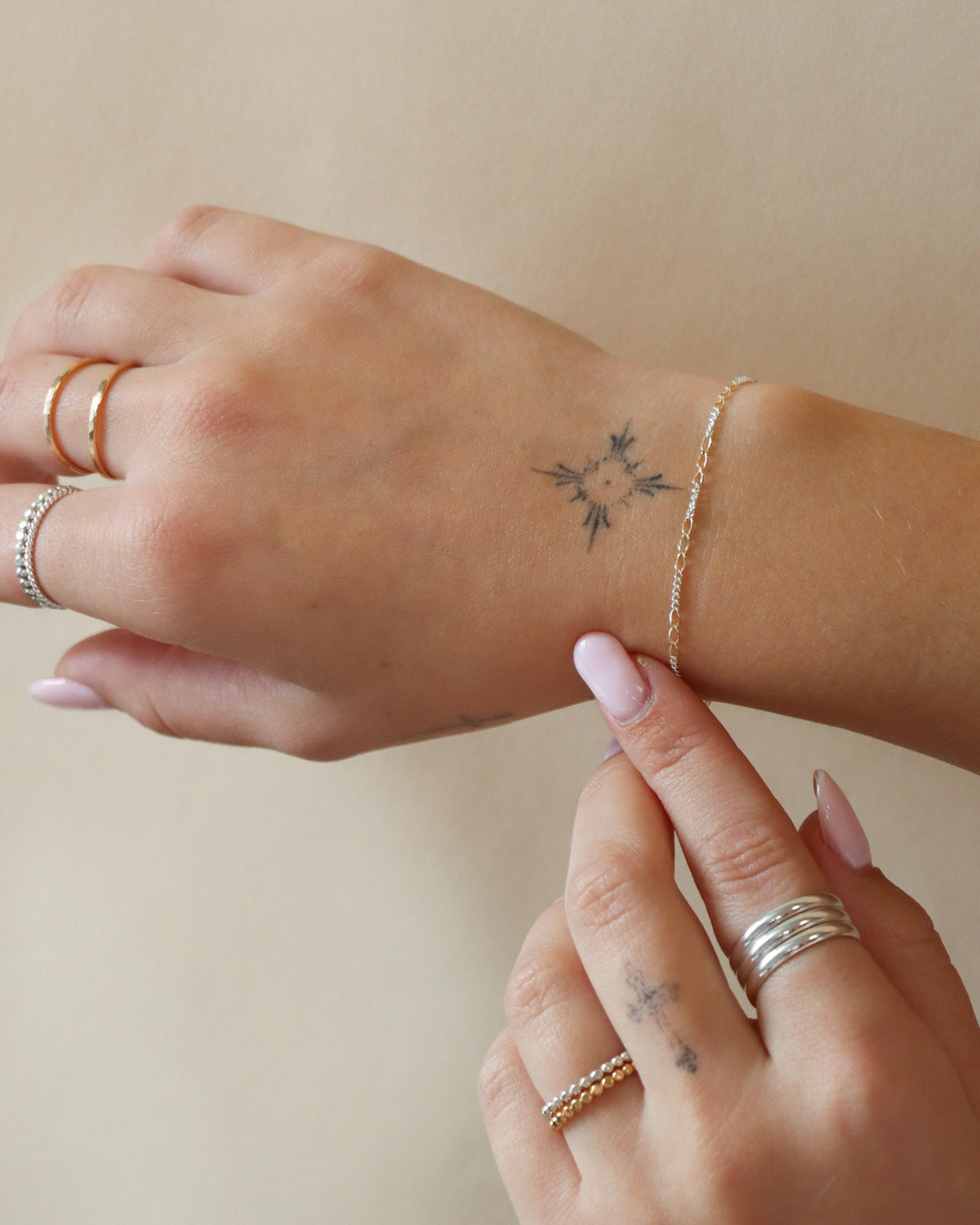 Close-up of Token Jewelry’s delicate mixed-metal Interlude Chain Bracelet featuring alternating gold and silver links, styled with stacked rings on a model’s wrist in soft natural light.