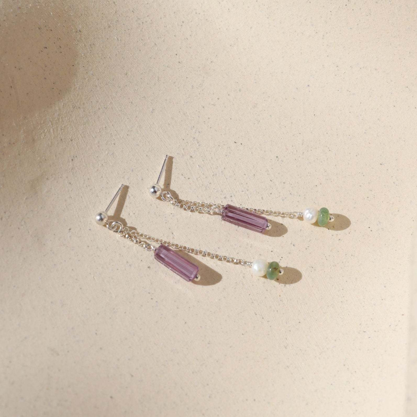 sterling silver stud earrings with chain, purple zircon tubes, pearls, and moss agate on a light background