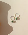 A sterling silver 14mm hoop with a Jade ball gemstone dangling from it. Earrings are displayed on a cream background. 