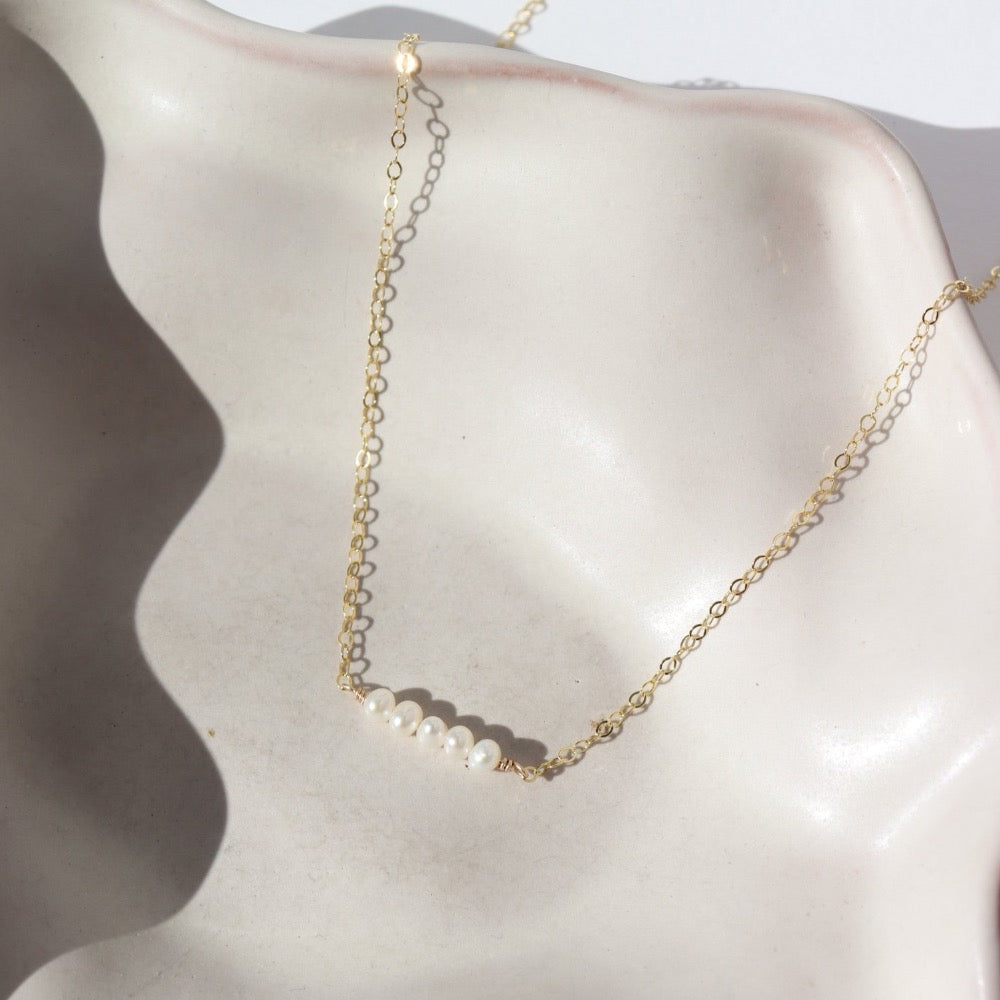 five freshwater pearls lined up on a 14k gold fill simple chain, made by Token Jewelry , photographed on a white ceramic dish