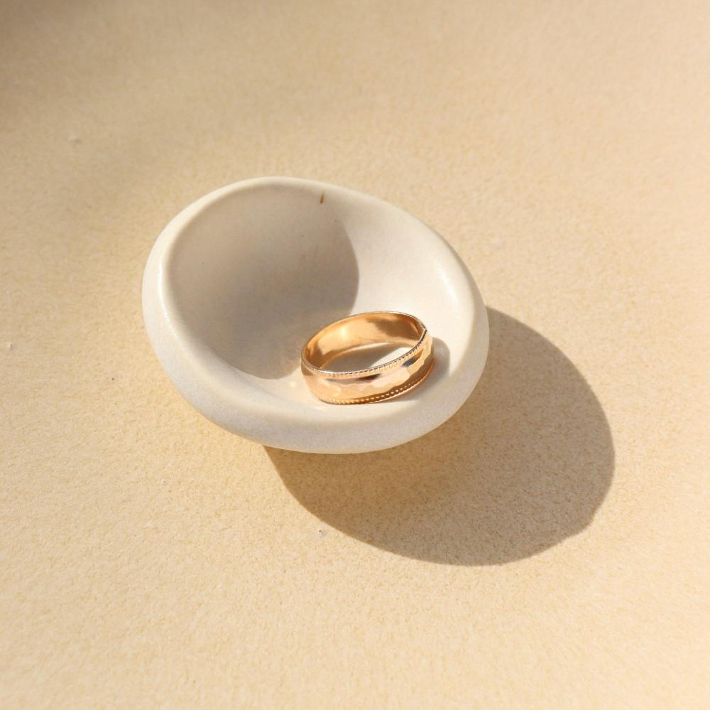 A gold hammered band with rippled edges. Displayed on a small ring dish. 