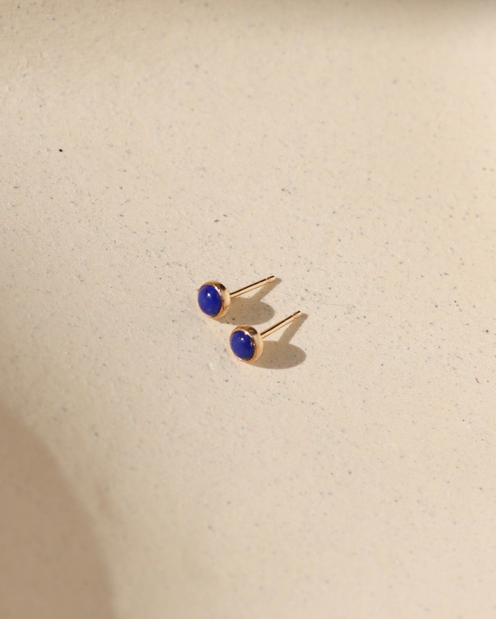14k gold fill bezel ear posts with 4mm lapis lazuli stones on a light background