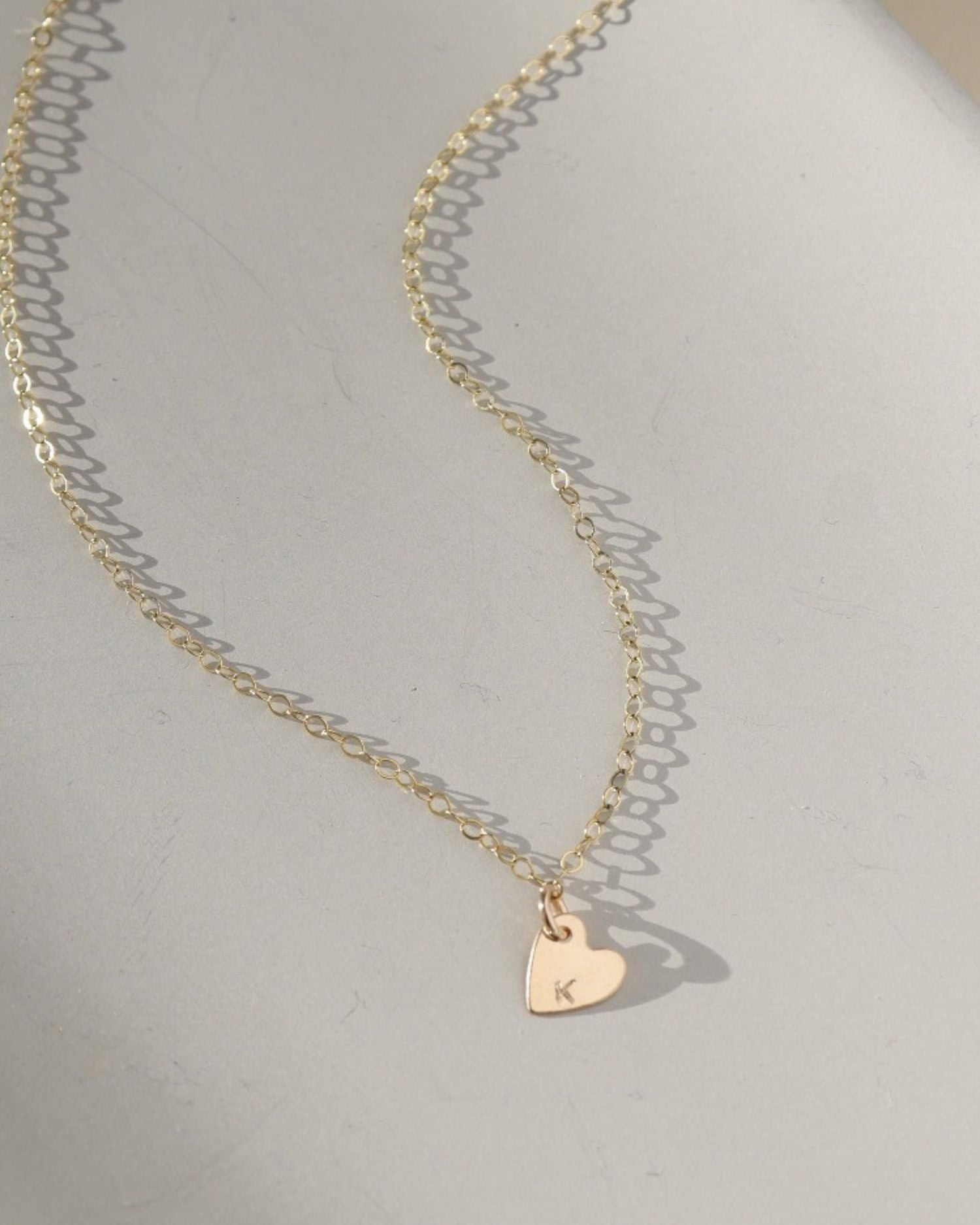 a dainty heart charm with an initial stamped on them, on a necklace chain, photographed on a ceramic dish