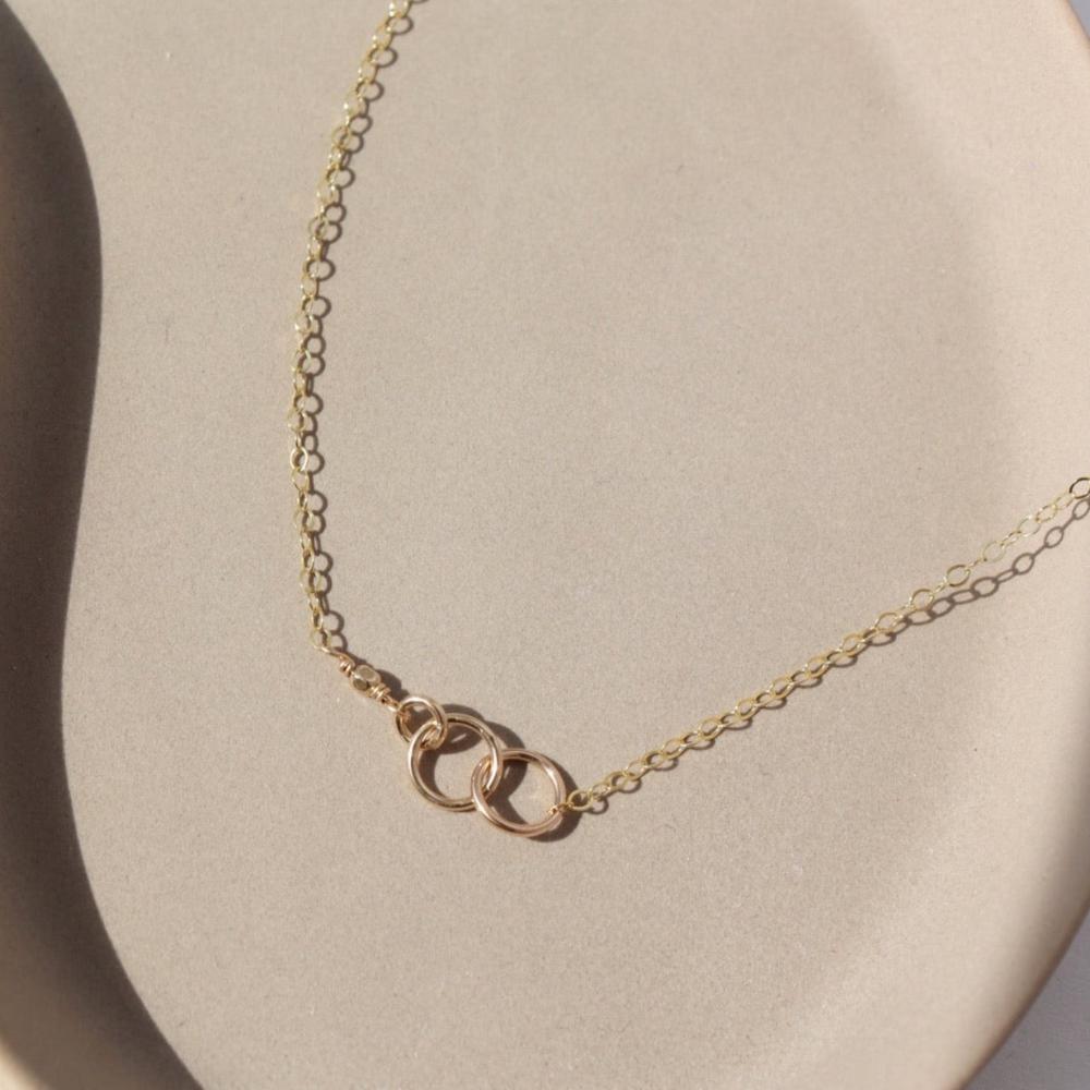 Lineage Necklace in 14k gold fill laid on a tan plate in the sunlight