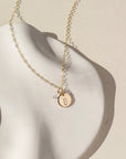 A 14k gold fill simple chain with a stamped disc with a small bunny, paired with a small opal wire wrapped gemstone. Necklace is displayed on a cream backdrop. 