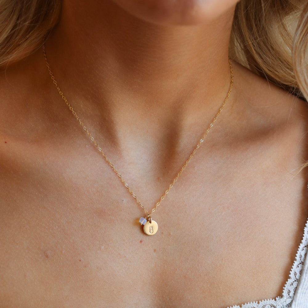 Model wearing a 14k gold fill simple chain with a stamped disc with a small bunny, paired with a small opal wire wrapped gemstone. 