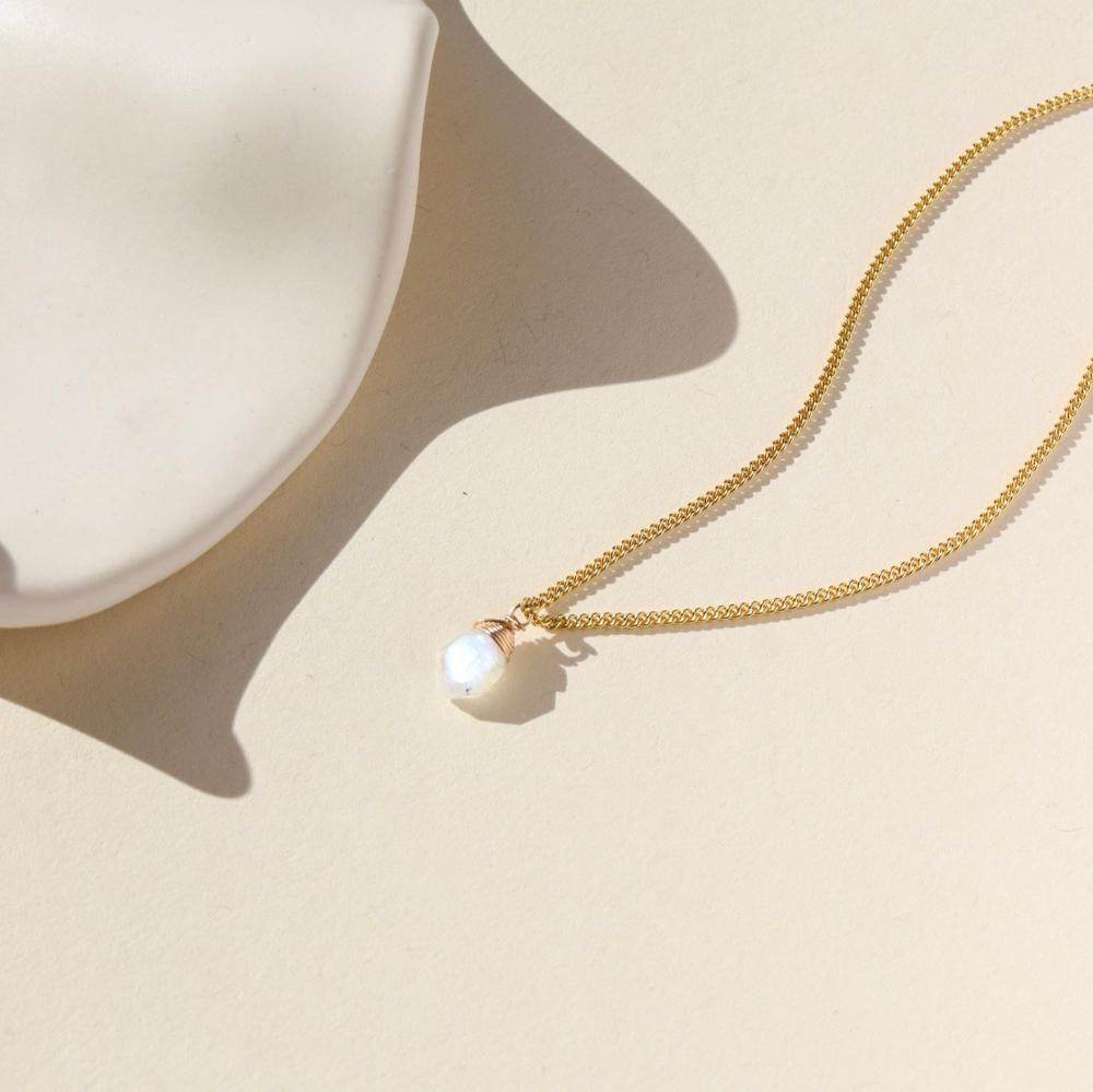 Delicate gold curb chain, with moonstone slice gemstone. Displayed on a cream backdrop. 