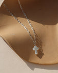 sterling silver paperclip chain necklace with mother of pearl cross pendant charm on a tan dish