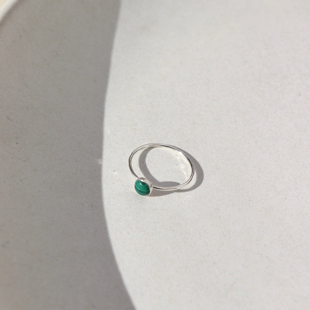 A sterling silver skinny band featuring a 5mm malachite stone set in a silver bezel. The 5mm Malachite Ring is displayed on a cream dish. 