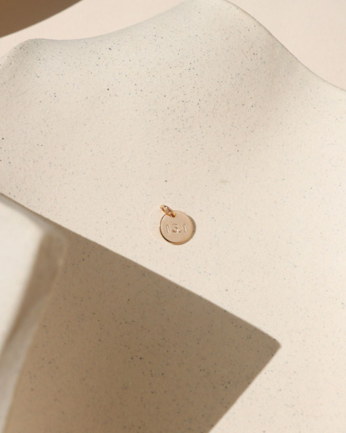 14k gold fill round disc with marathon miles hand stamped on it on a light dish