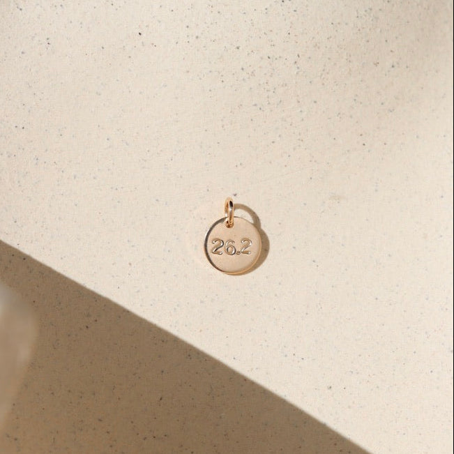 14k gold fill round disc with marathon miles hand stamped on it on a light dish