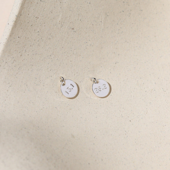 sterling silver round discs with marathon miles hand stamped on it on a light dish