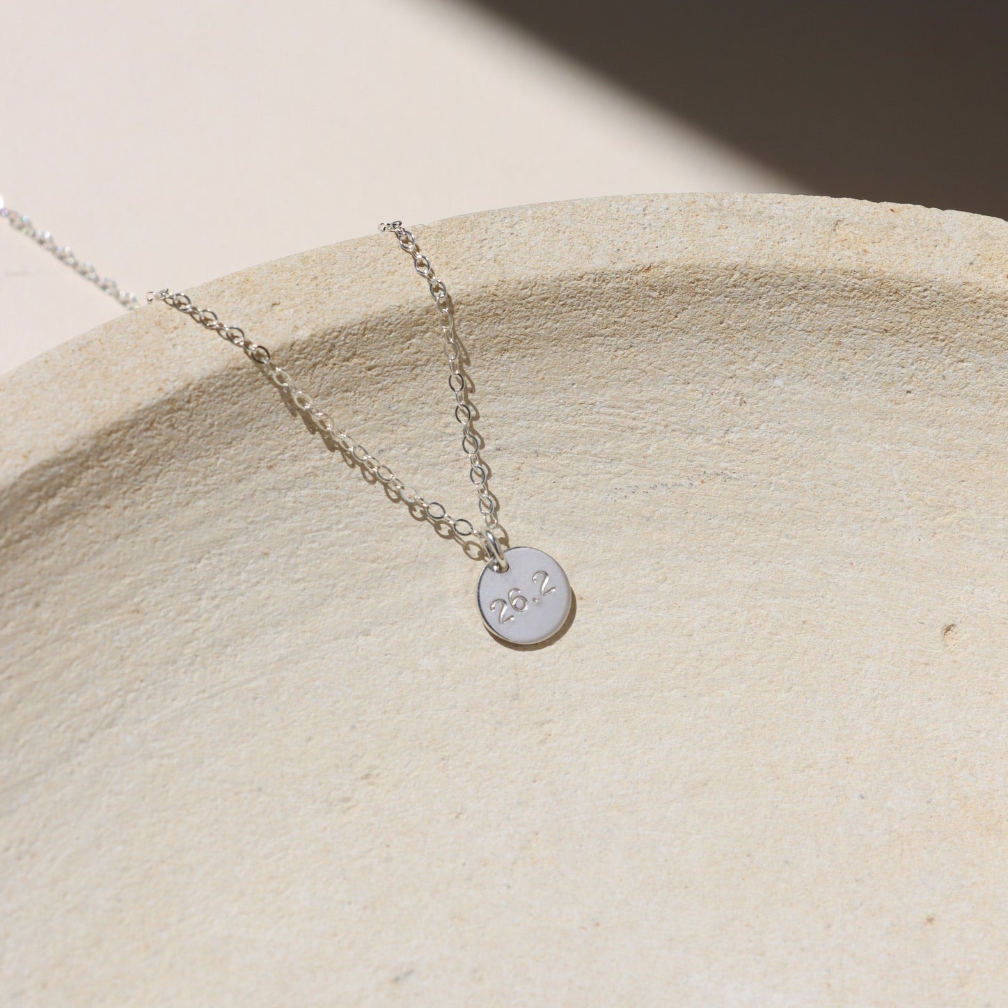 sterling silver hand stamped round disc charm on a delicate chain necklace on a light surface